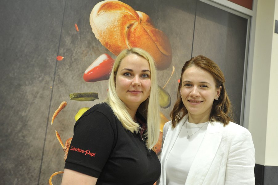 Eine junge Frau mit blonden Haaren in Leberkas-Pepi-T-Shirt udn eine junge Frau mit braunen Haaren im weißen T-Shirt und Blazer