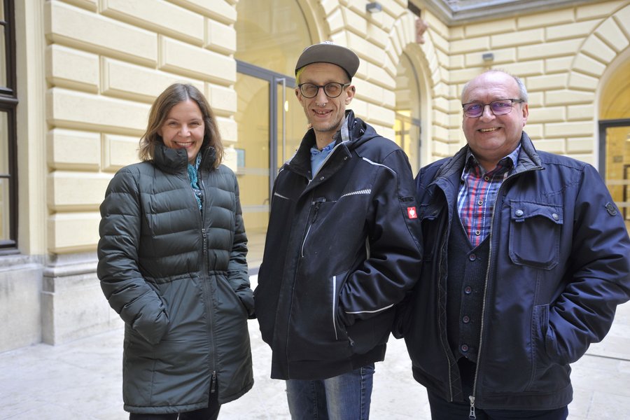 Eine Frau und zwei Männer, einer davon mit Schirmkappe und Piercings, in einem Hof der Universität Wien